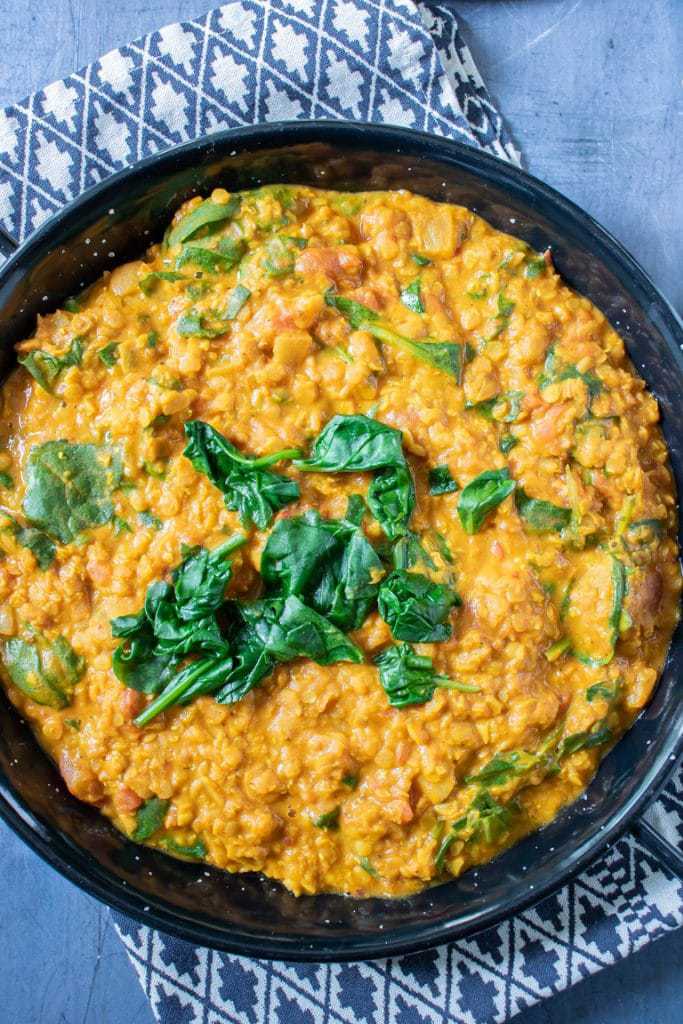 Red lentil dhal in a black dish with a small pile of freshly wilted spinach. Vegan, vegetarian, gluten free recipe. 