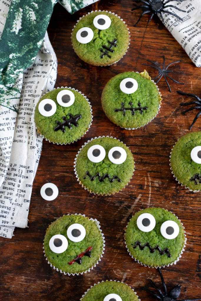 Wooden background with overhead shot of halloween cupcakes - this recipe makes naturally bright green cupcakes - with spinach. You can't taste it but they are a great hidden vegetable cake. 